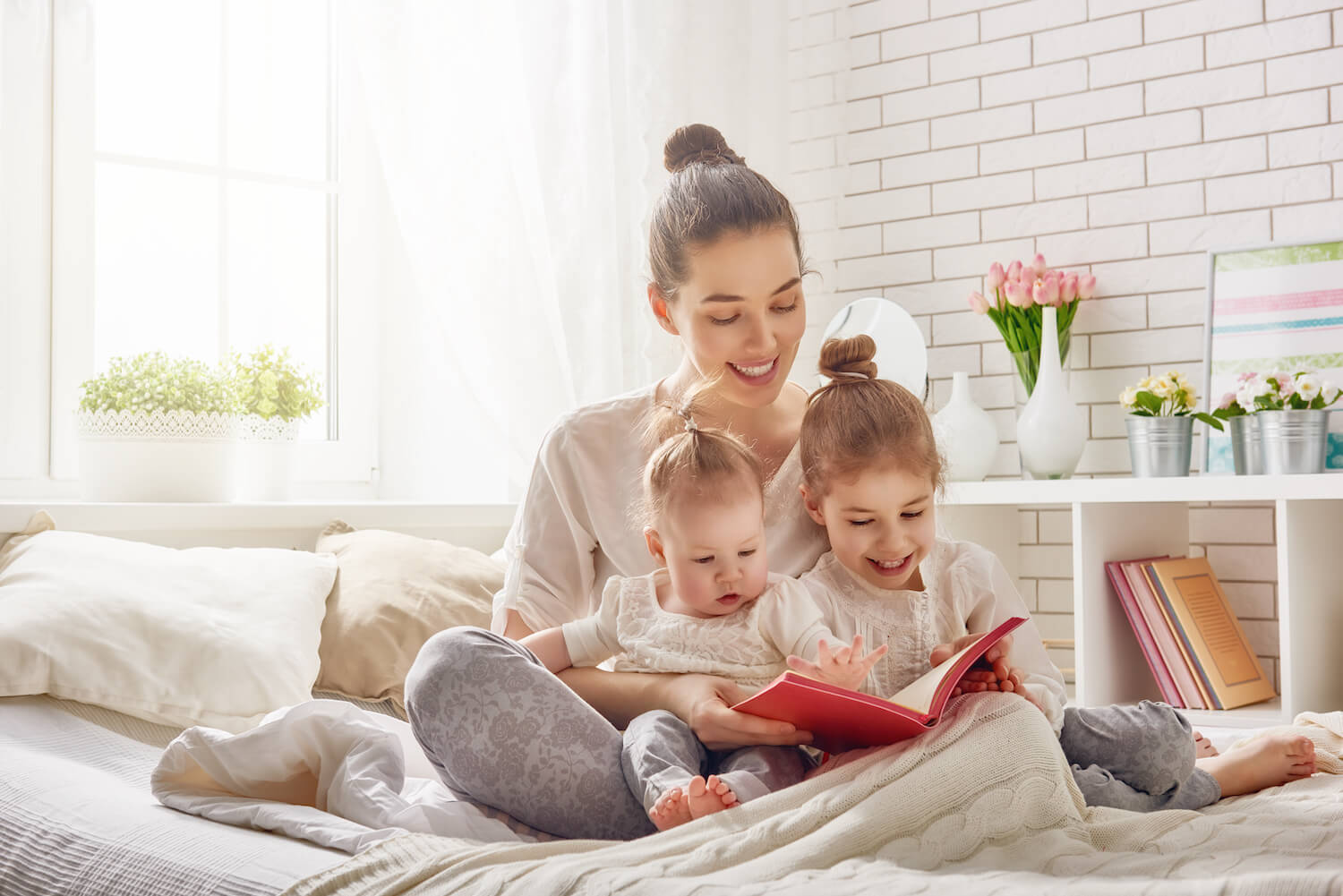 interior shot of mother reading a book to her 2 infant children on a bed