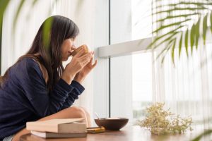 close up angled shot of woman drinking from mug staring out a window